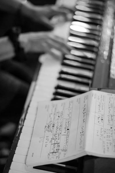 Hand jamming on a piano with chord sheets resting on the side